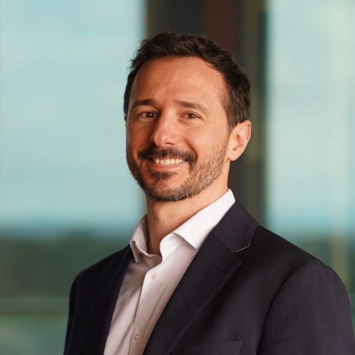 Male researcher with dark hair wearing a white shirt and black jacket and smiling.