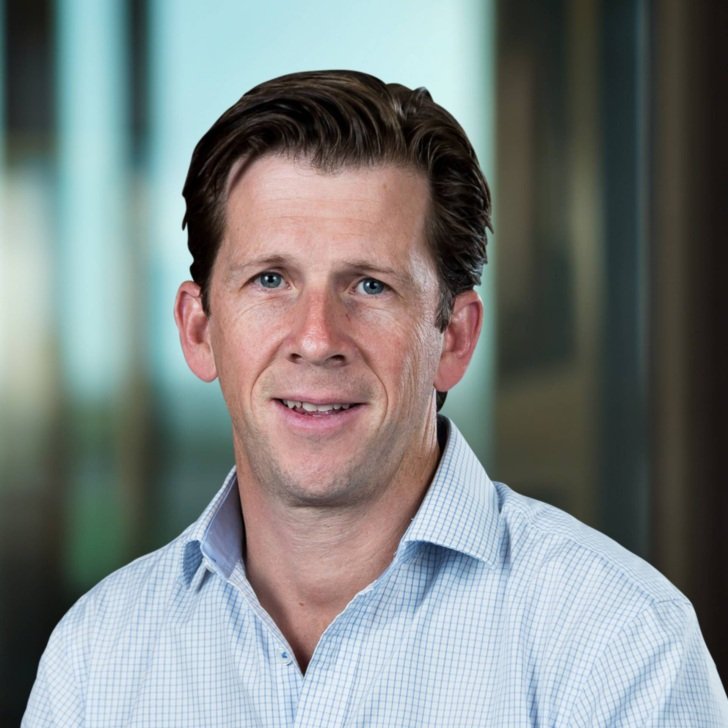 Man with brown hair wearing a light blue and white checked collared shirt