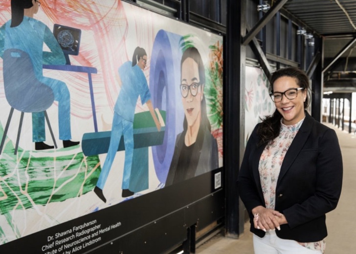 Dr Shawna Farquharson standing in front of the mural depicting her as part of the Metro Tunnel Creative Program.