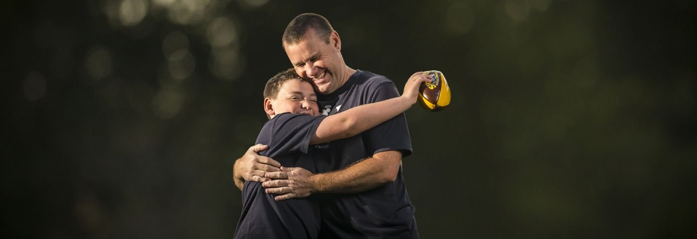 A man hugs his young son who is holding a football