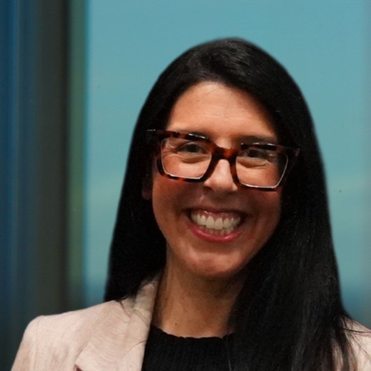 Woman with long dark hair and large brown glasses wearing a beige jacket