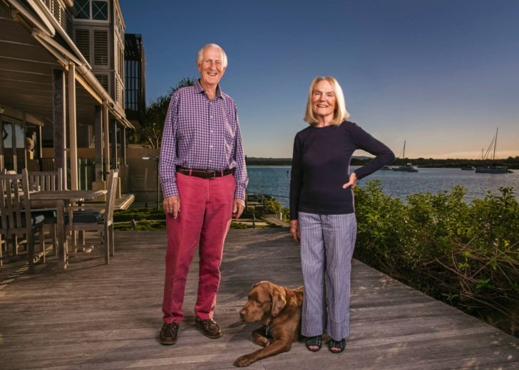 Carl and Wendy Dowd. They stand on a deck overlooking the bay. Their pet dog sits at their feet.