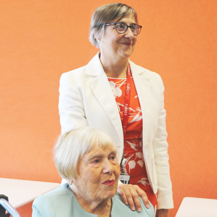 Professor Julie Bernhardt poses with hand on Rhonda Hall's shoulder against orange background
