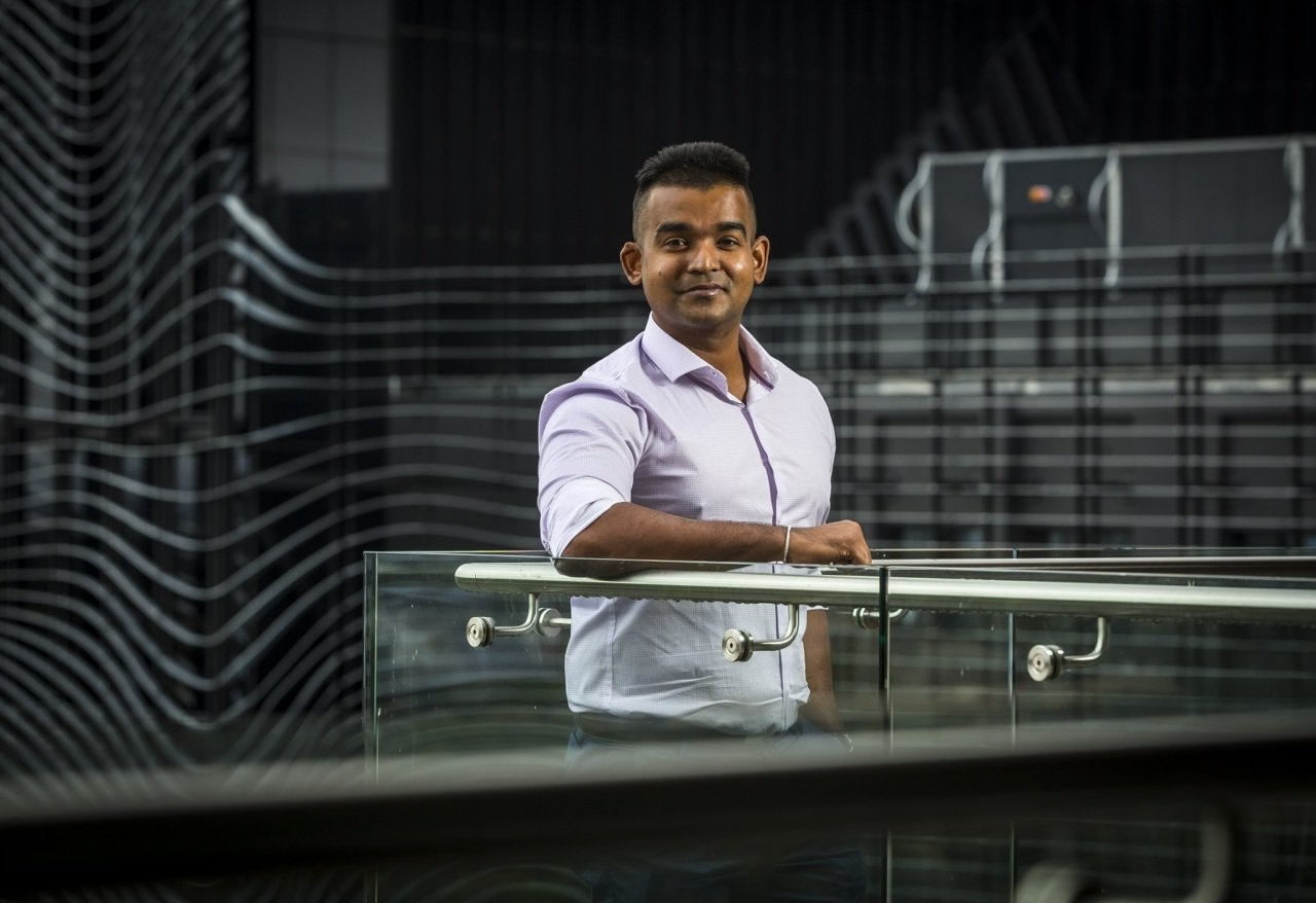 Associate Professor Yugeesh Lankadeva leans on a balcony with a black building as a backdrop