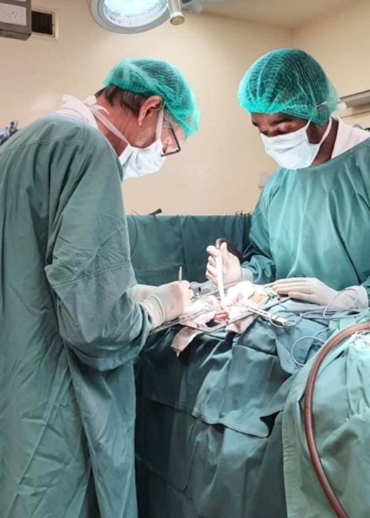Two researchers conducting a surgery in full surgical scrubs, masks and hairnets