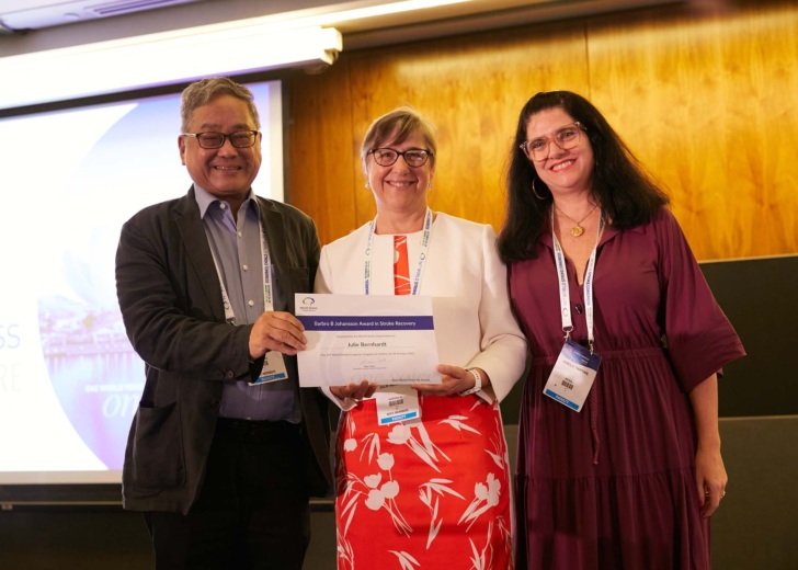 Professor Julie Bernhardt stands holding an award between two colleagues at the world stroke congress event