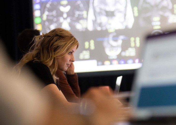Female resarcher stares intently at laptop screen during meeting - MRI scans displayed behind her