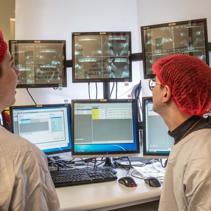 Researcher in red hair net and lab coat sits in front of 6 screens monitoring animal model behaviour