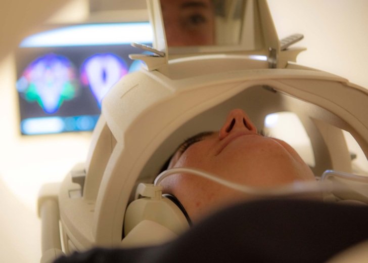 Patient sits within an MRI scanner with MRI imagery on screen in background