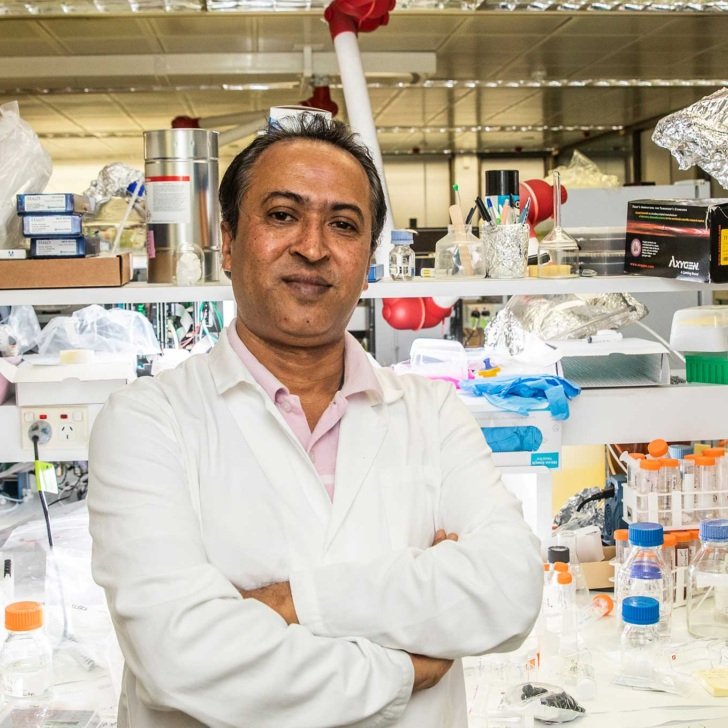 Professor Akhter Hossain standing with arms folded with laboratory equipment in the background.