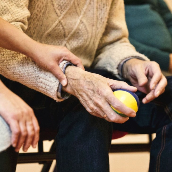 Elderly man sitting on a chair and holding a small ball in his right hand.