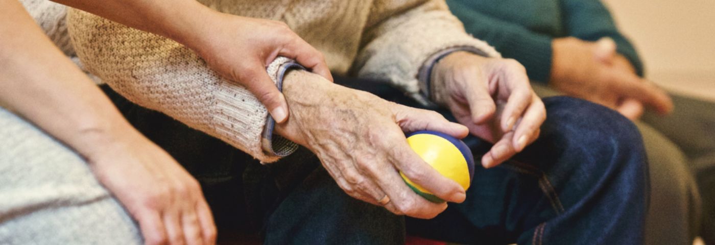 Elderly man holding a small ball in his right hand.