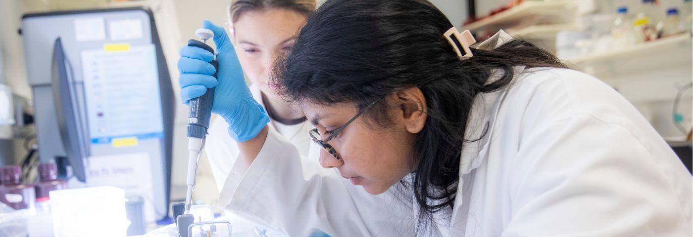 Young woman researcher with dark hair and glasses holds a pipette.