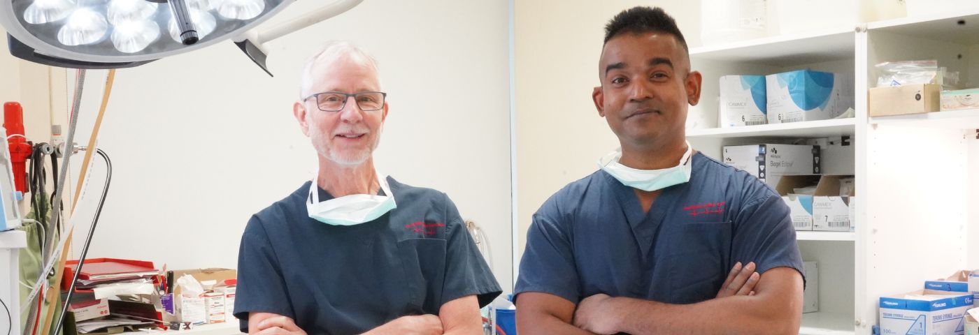 Professors Clive May and Yugeesh Lankadeva in a Florey laboratory. They wear dark blue surgical scrubs and are standing with their arms crossed.