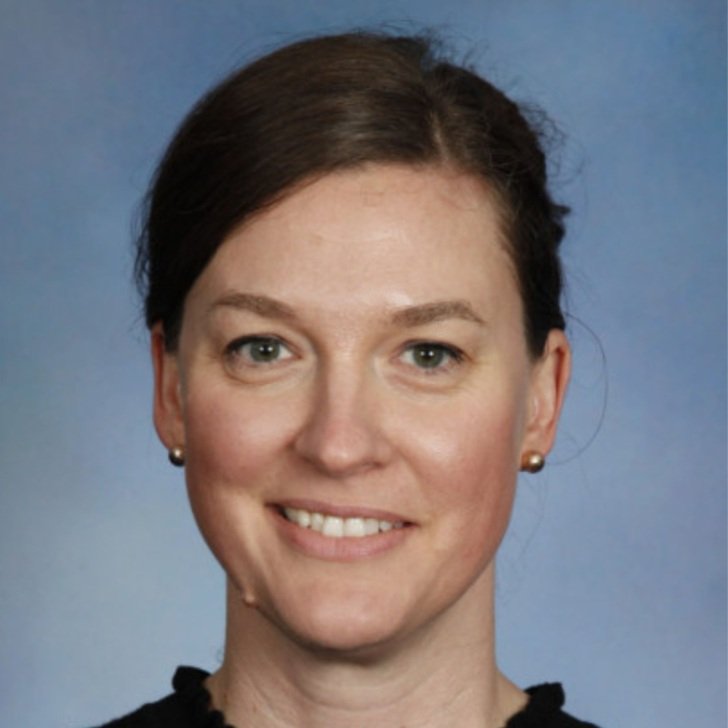 Woman with dark hair tied back and wearing small gold earrings