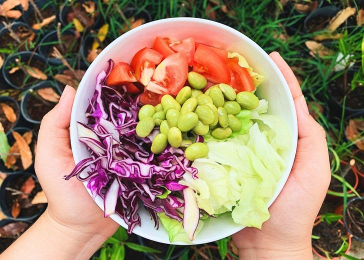 A pair of hands holding a bowl of sliced vegetables