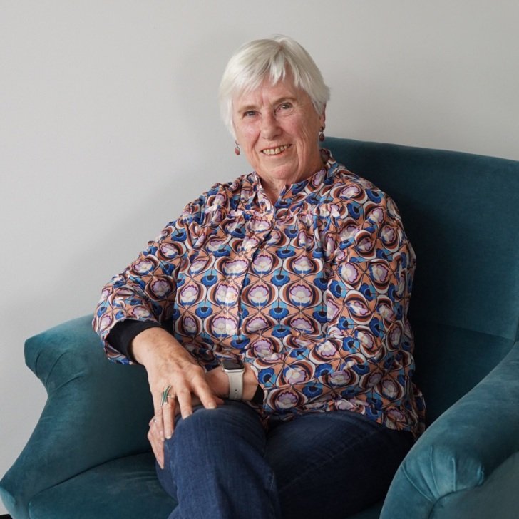 Older woman with grey hair sitting in a green chair and smiling