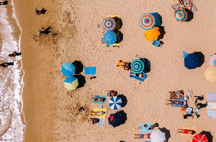 An aerial view of a beach and water with several brightly coloured umbrellas