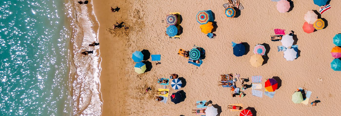 An aerial view of a beach and water with several brightly coloured umbrellas