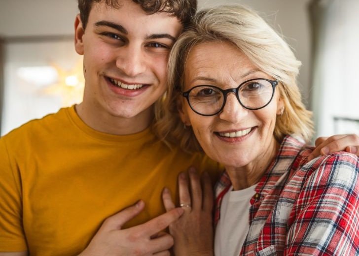 Mother and son smiling at the camera. They are holding each other.