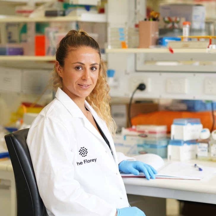 Scientist wearing lab coat rests hand on laboratory bench