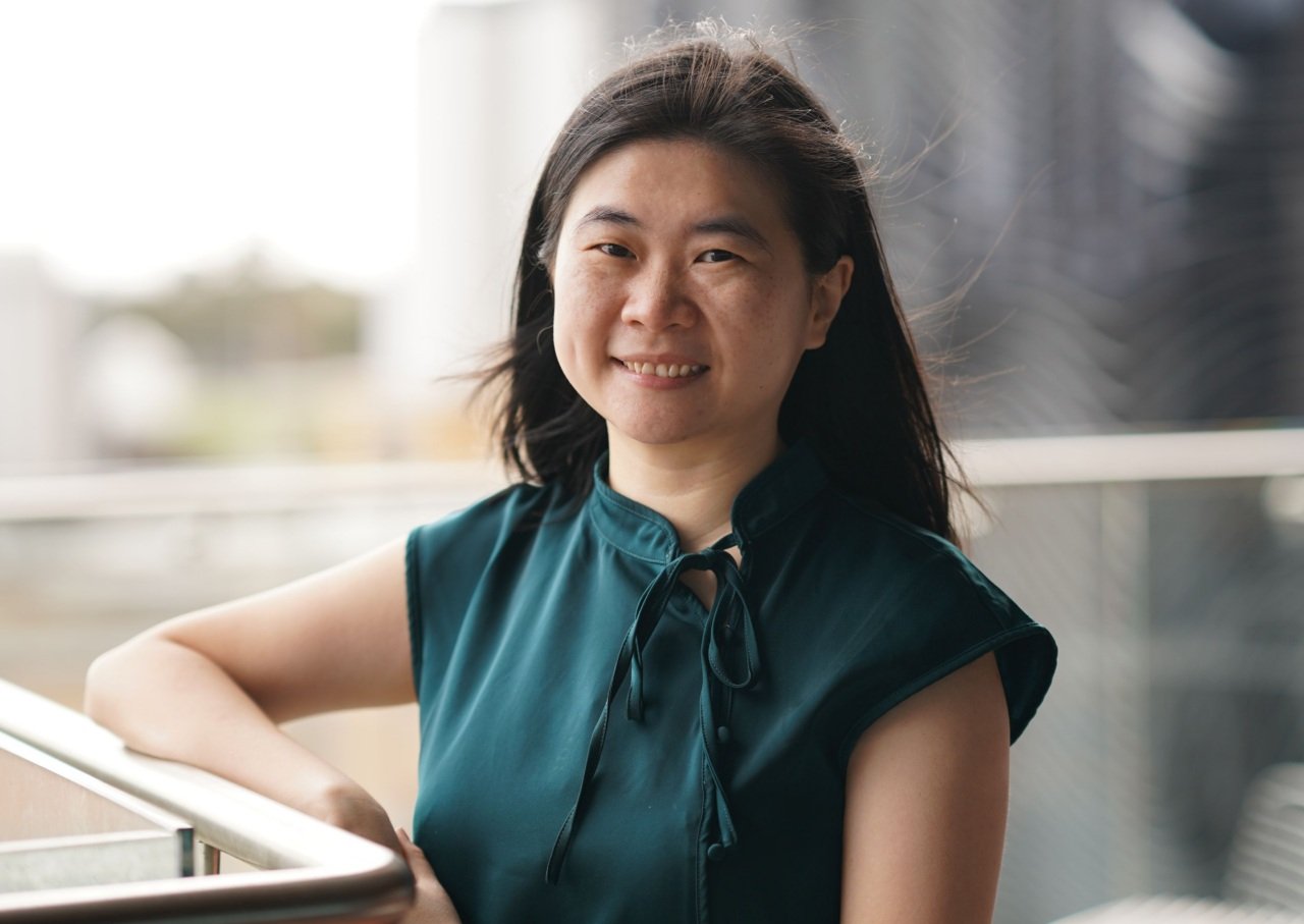 Woman wearing green shirt and smiling leans against handrail outside building