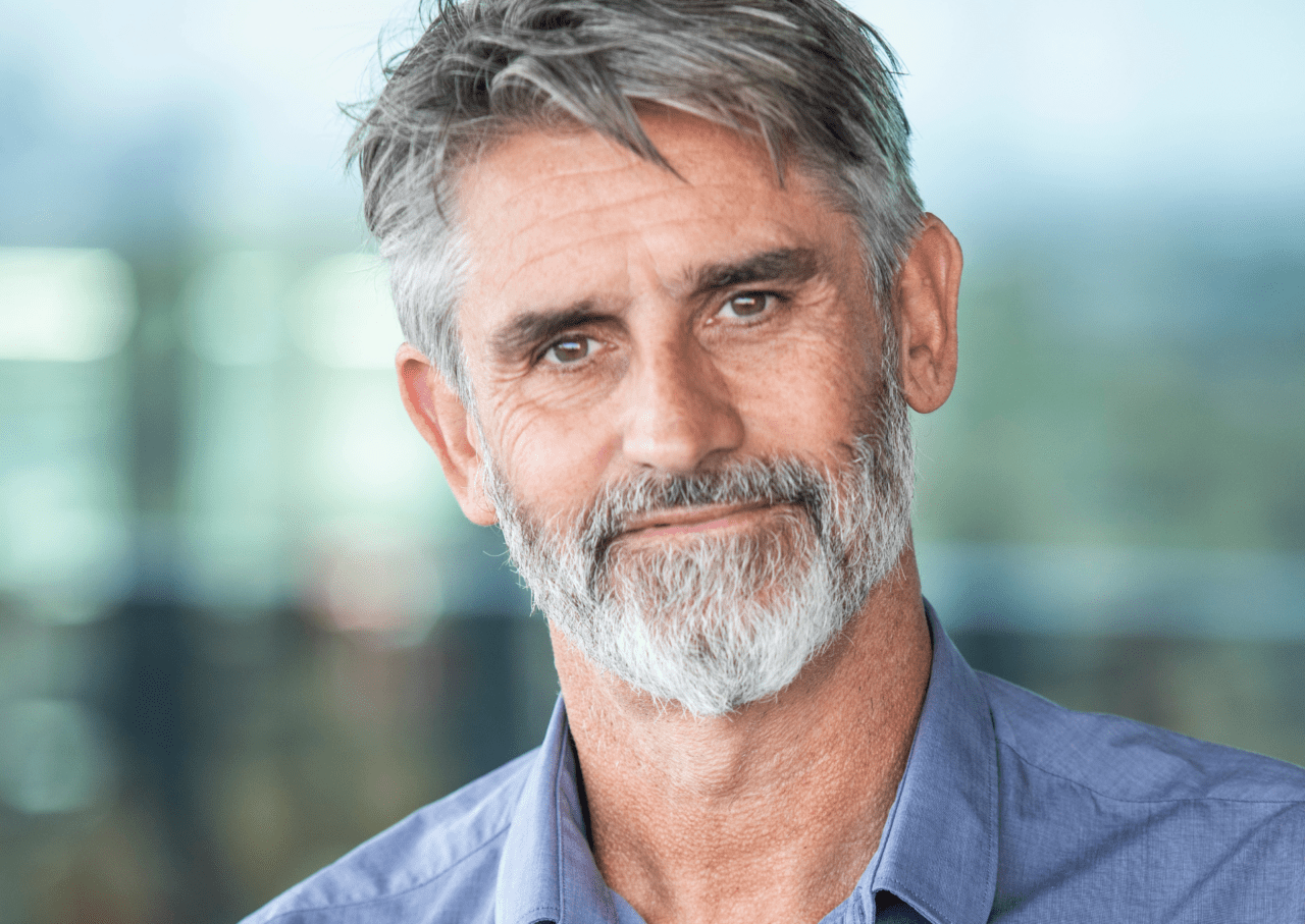 Man with facial hair wearing grey shirt smiles at camera