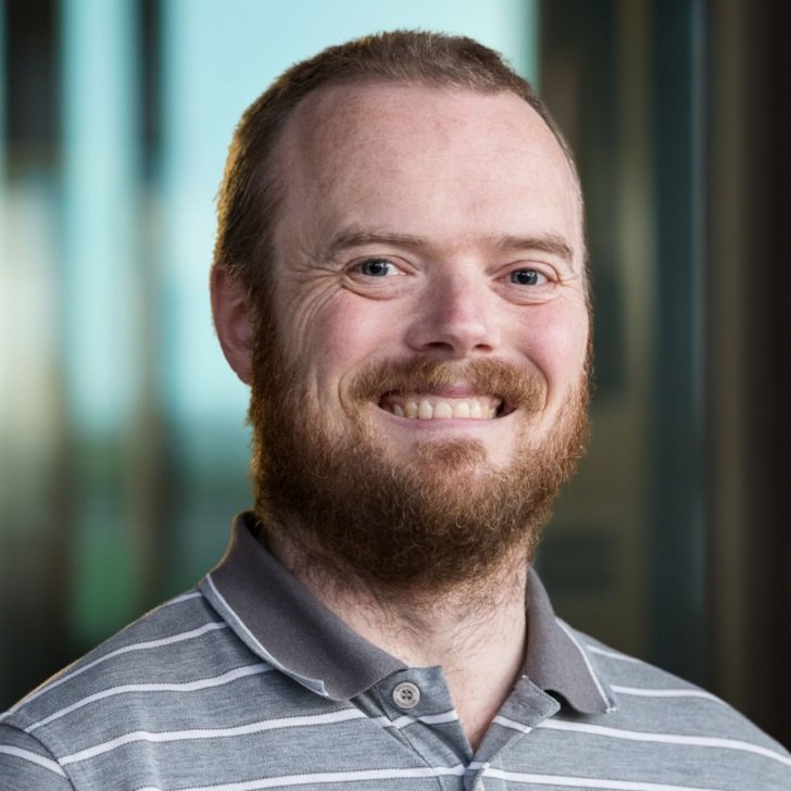Man with beard wearing striped grey shirt smiles