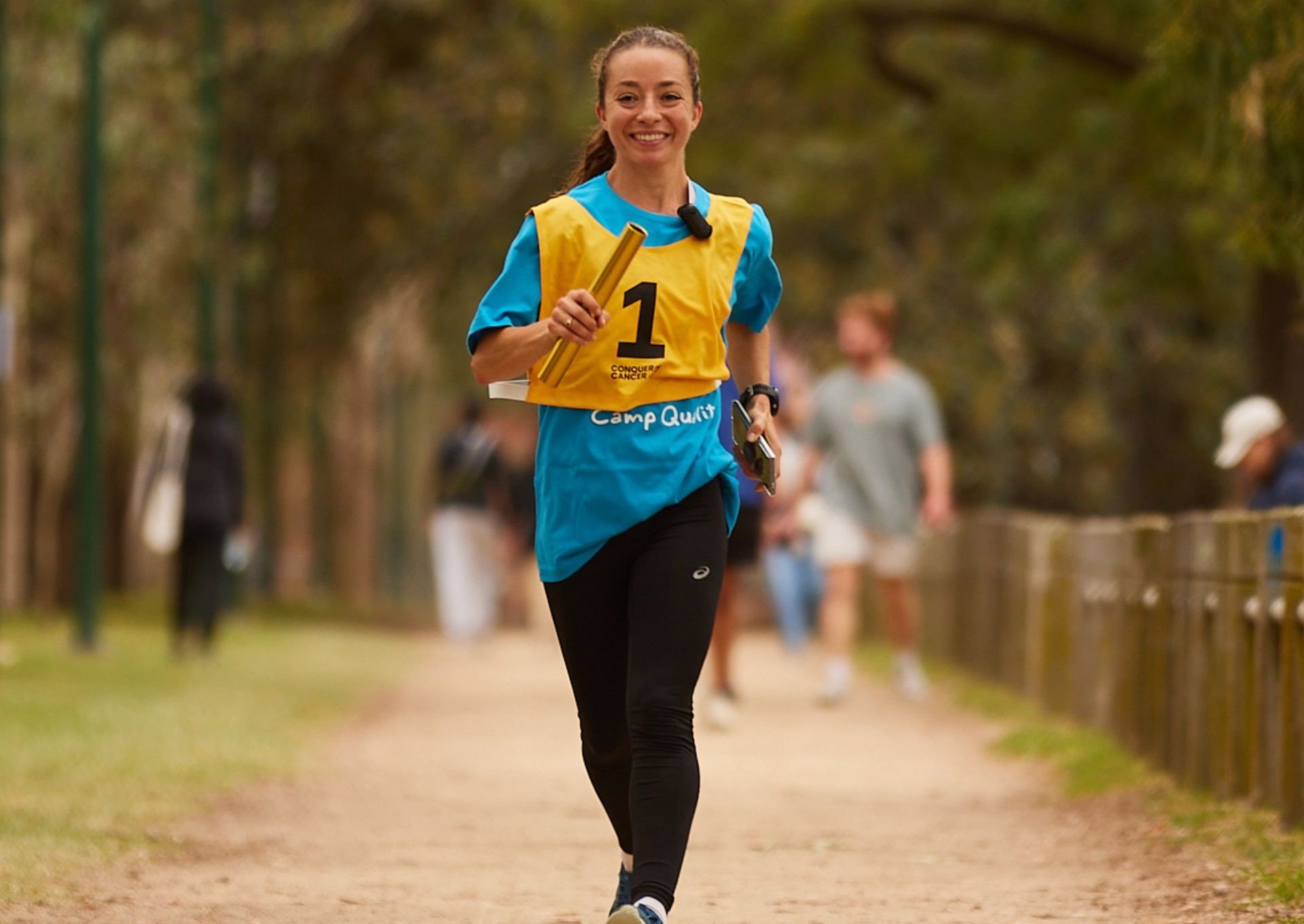 Woman wearing yellow running bib smiles while speed-walking around park