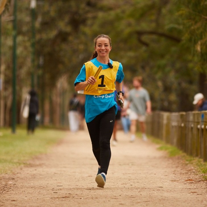 Woman wearing yellow running bib smiles while speed-walking around park