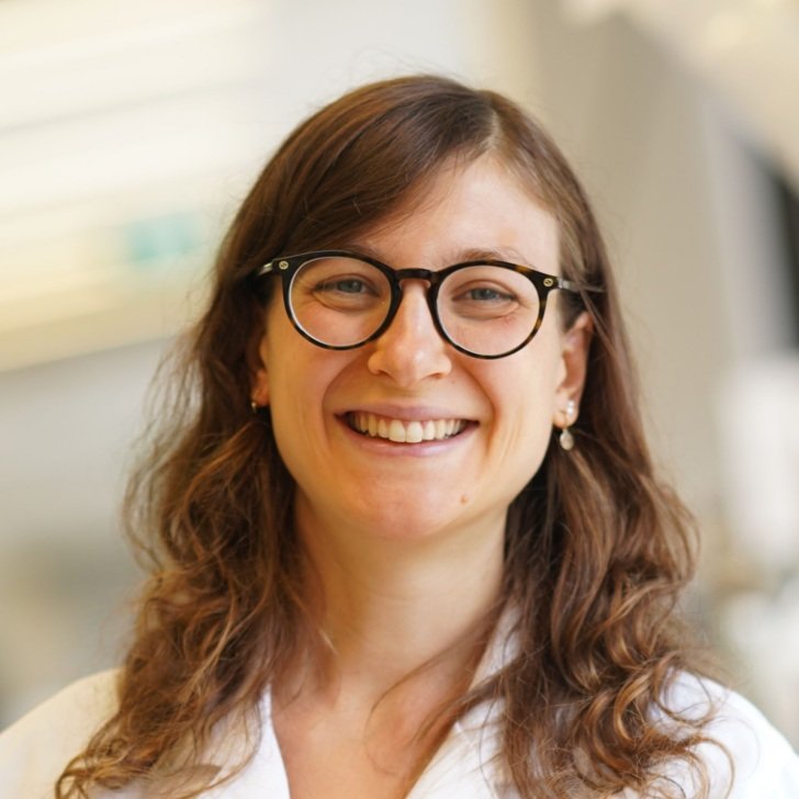 Woman wearing glasses and lab coat smiles
