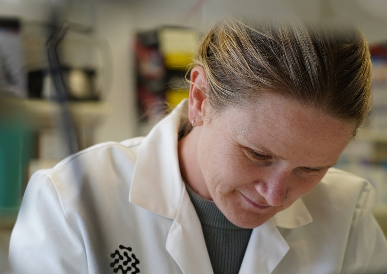 Scientist wearing lab coat looks down at lab bench while working