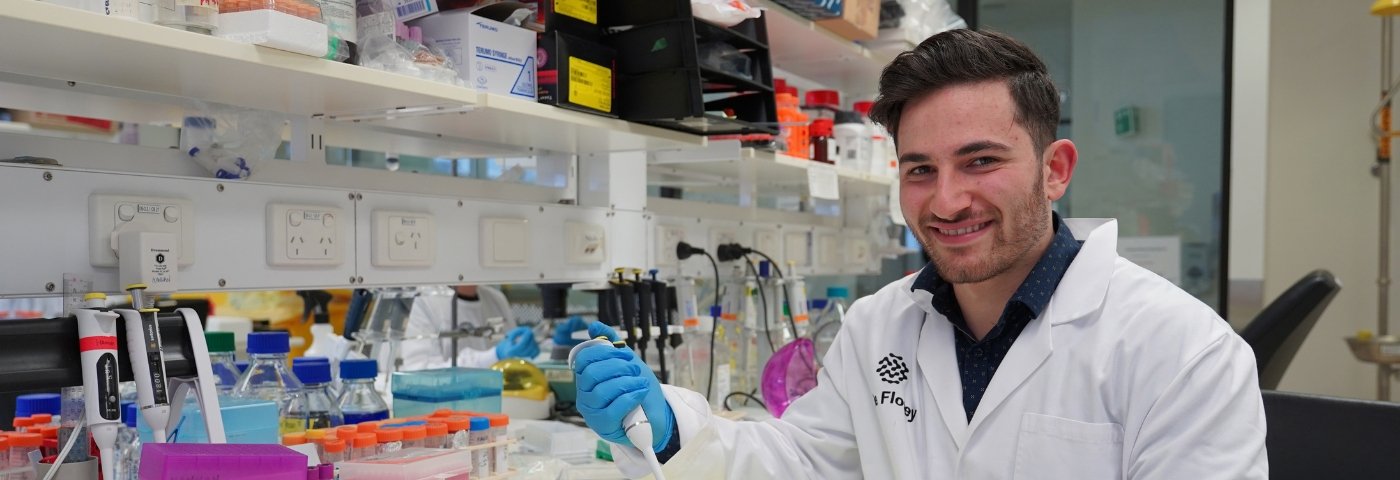 Scientist smiling while sitting at lab bench holding a pipette