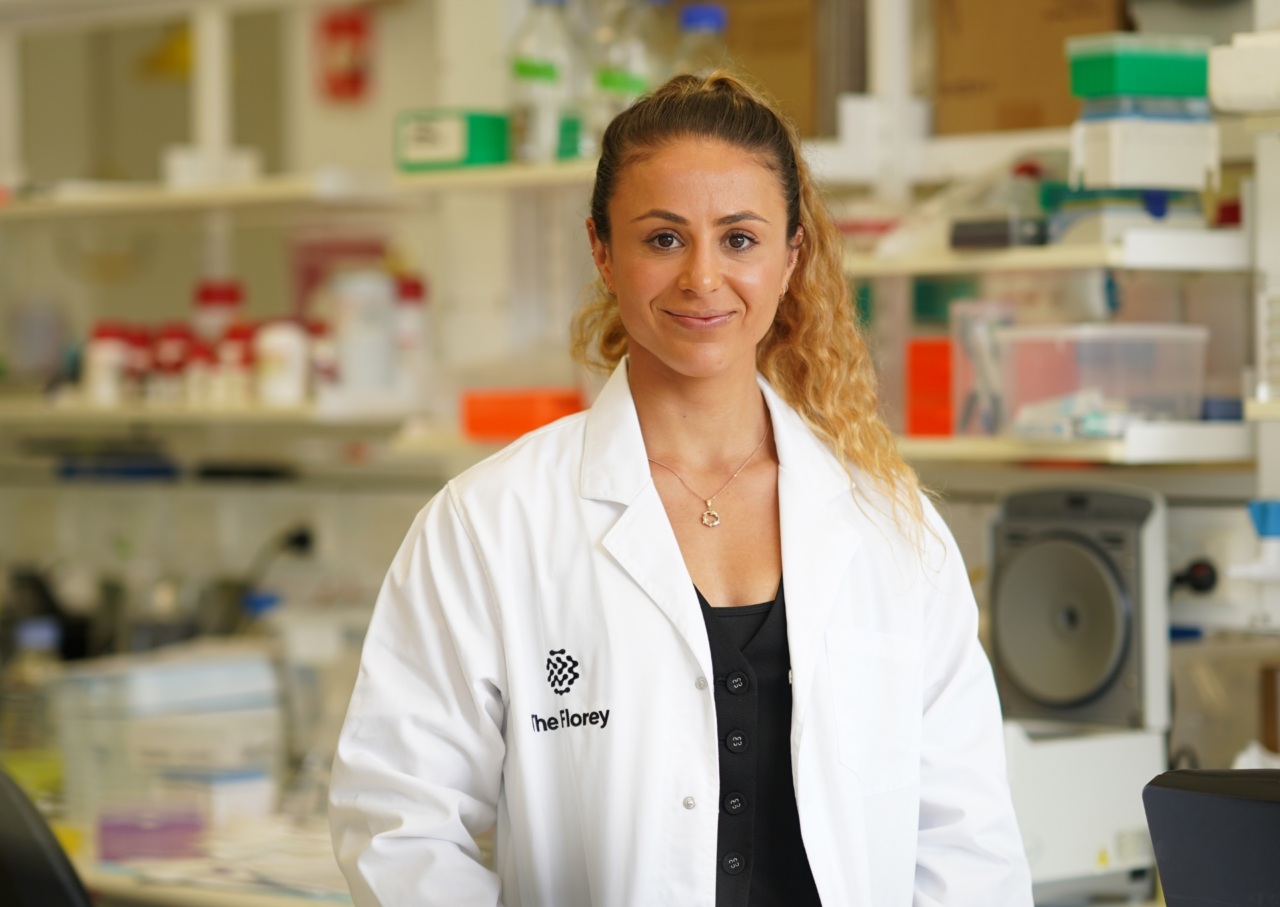 Woman wearing white lab coat stands in research lab, smiling